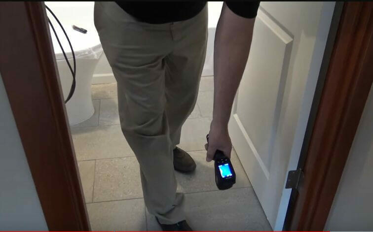 A person performing a test on the bathroom floor using a temperature sensor tool