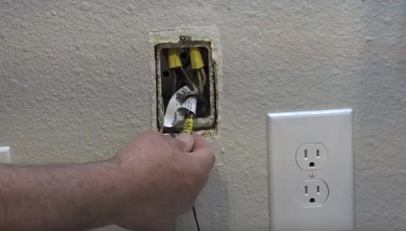 A person checking the wiring of thermostat mounted besides an outlet