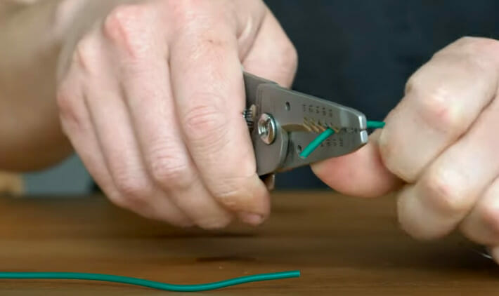 A person cutting a green wire using wire cutter tool