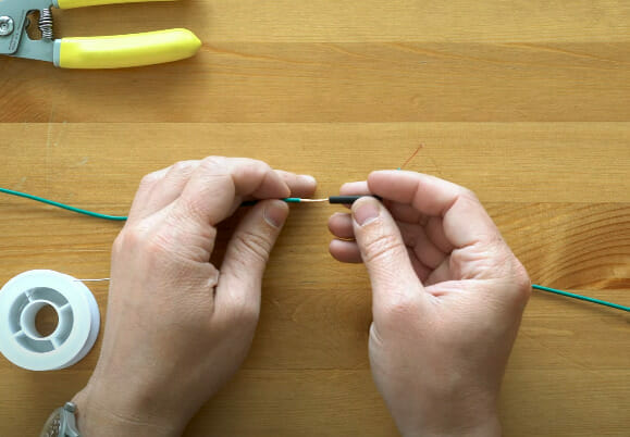 Understanding the process of wire conductor coating using solder through hands holding wire and scissors.