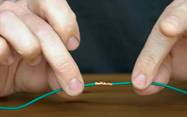 A person securing the two green wire's edges by twisting them together