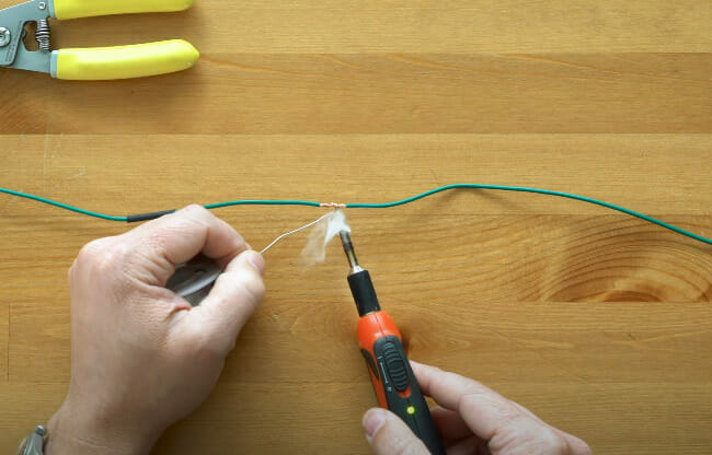 A person begins to solder the two green wire together