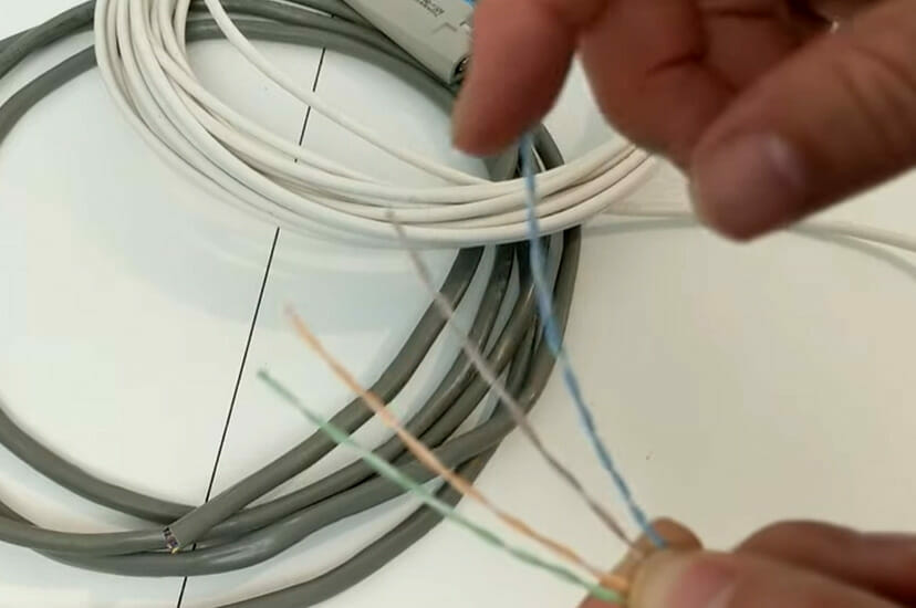 A person holding 4 strands of wires with grey and white rolled wires on the floor