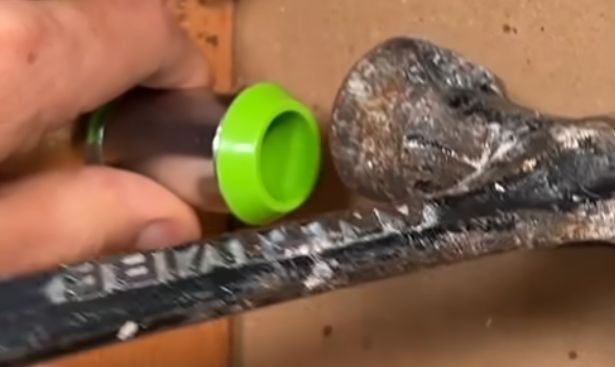 A person is placing the adjustable end of a hole protector and tapping it using a hammer