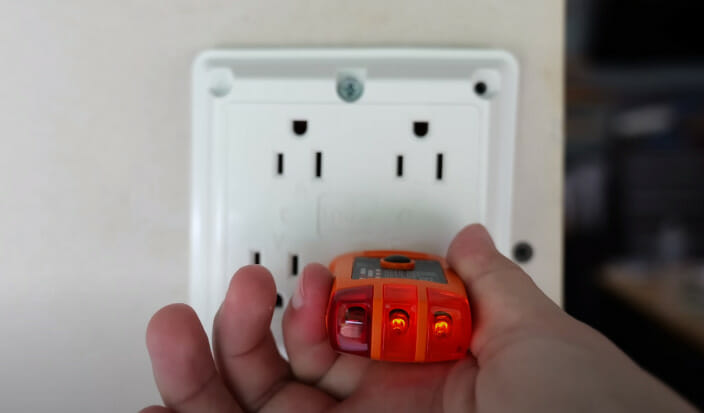 A person testing the voltage of a double outlet on the wall using a voltage tester tool