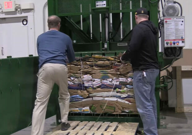 Two men loading a pallet a pile of boxes into a machine