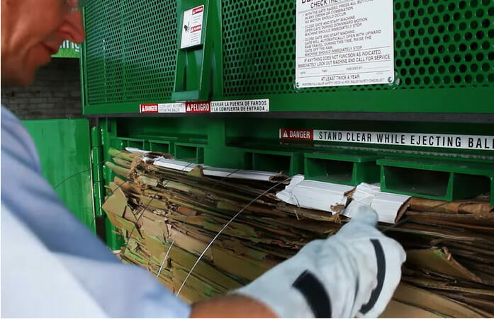 A man is using baling wire to put paper into a recycling machine