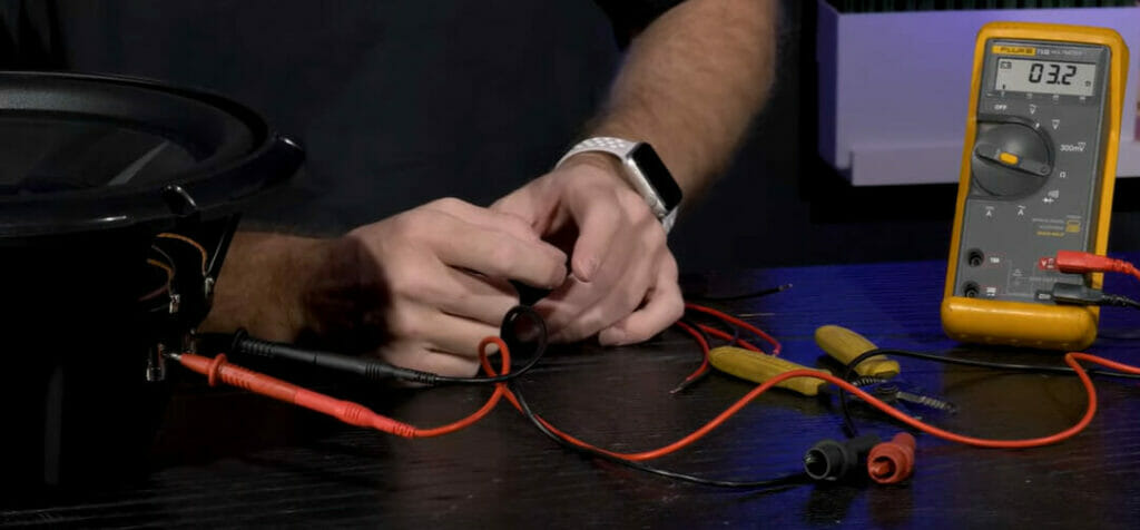 A man is using a multimeter to test a speaker and wire dual voice coil subs