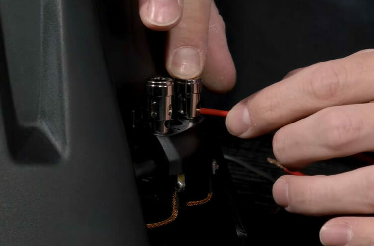 A person is inserting the red wire into a dual voice coil subs