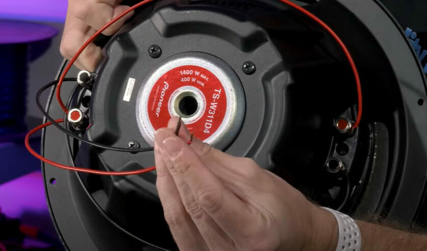 A person is holding a black and red wire to wire the dual voice sub