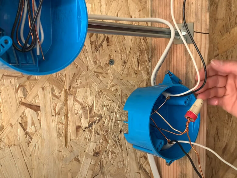 A person is capping off the wires with wire nut in a blue electrical box