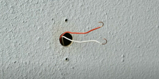 A hole in the wall with red and white wires in it