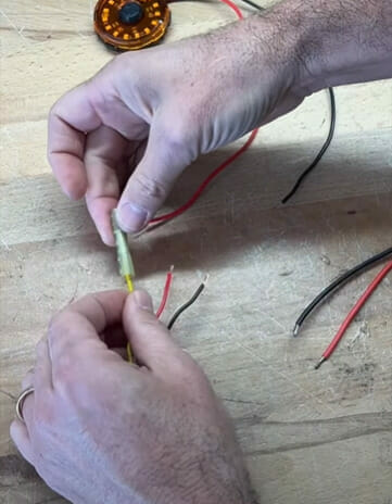 A man is connecting wires to a rocker switch on a wooden table