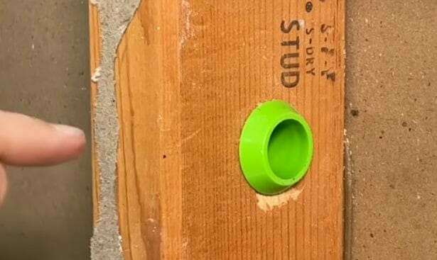 A person is pointing at the green hole protector at is installed at the stud hole