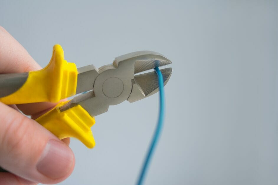 A person cutting a blue wire with a wire cutter