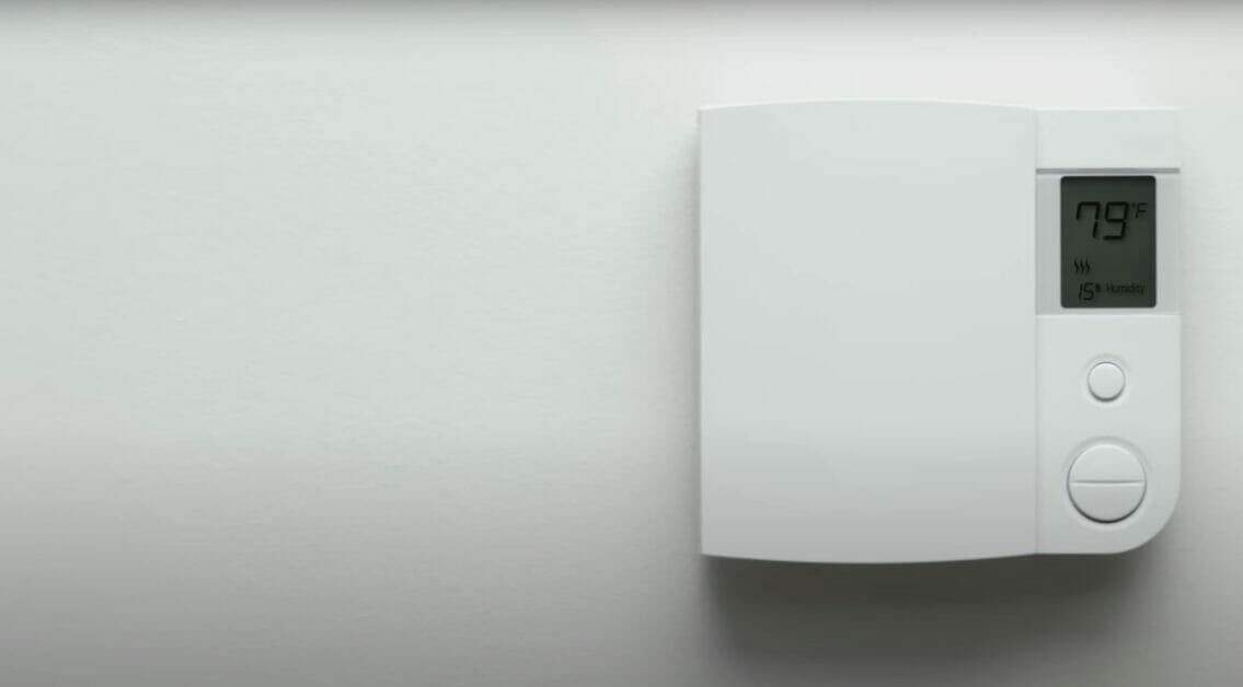 White thermostat showing 79f temperature on a white wall