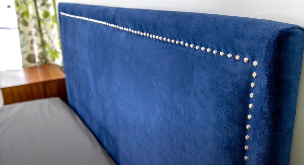A blue headboard cushion with nailhead trim upholstery