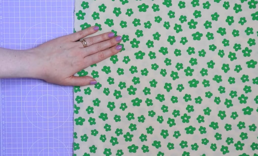 A woman's hand touching two different fabric in purple and green little flower design