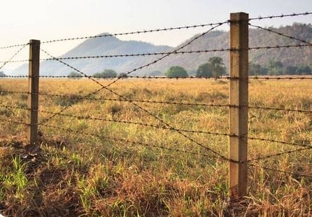 A barbed wire fence built in a field with mountains in the background.