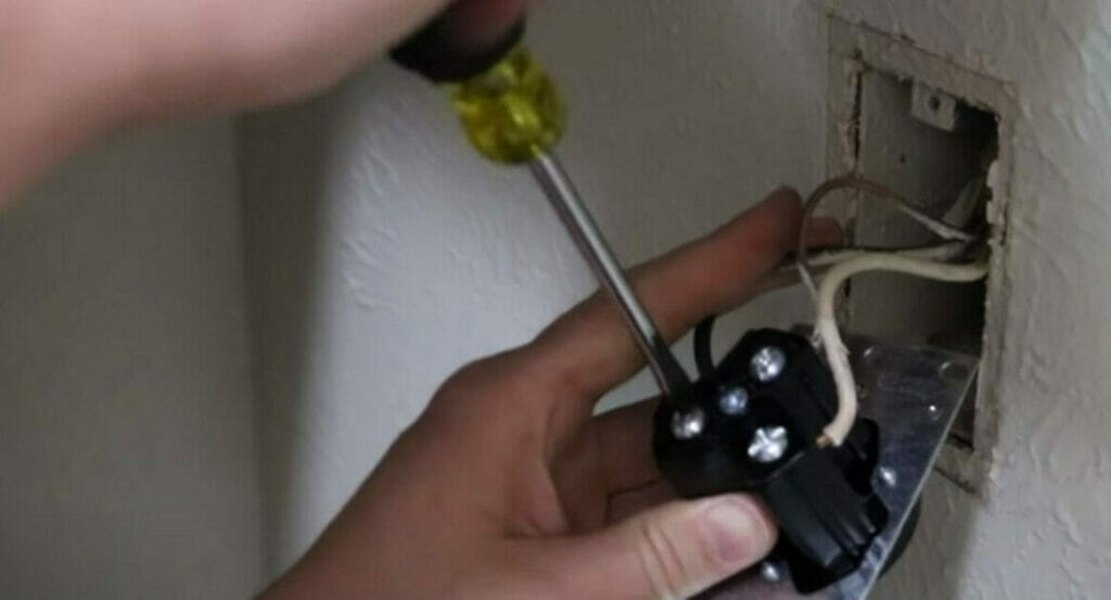 A person attaching the black (hot) wire to the brass screw