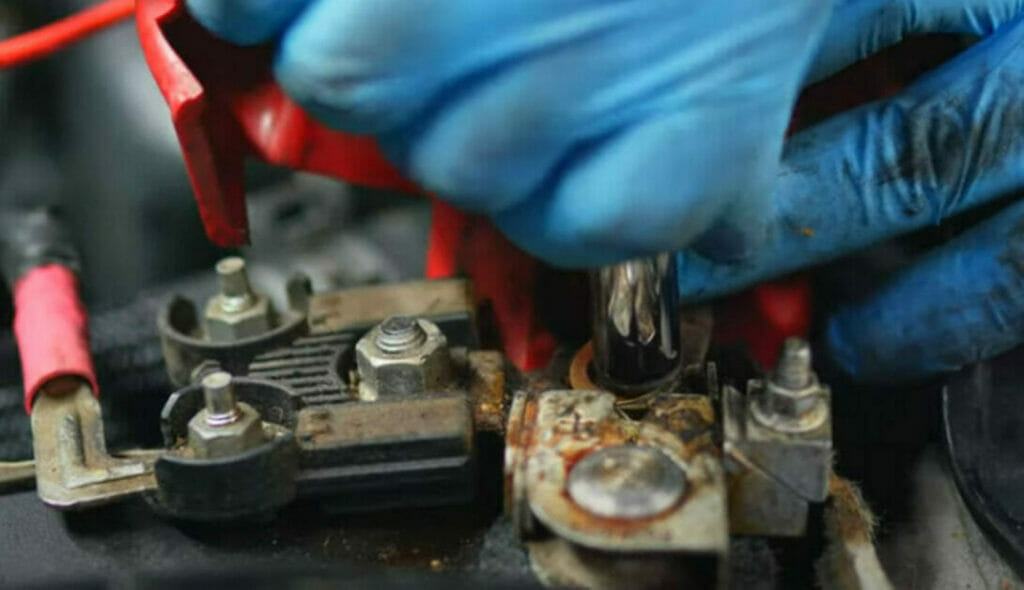 A person wearing blue gloves attaching ring terminals of harness to battery terminals