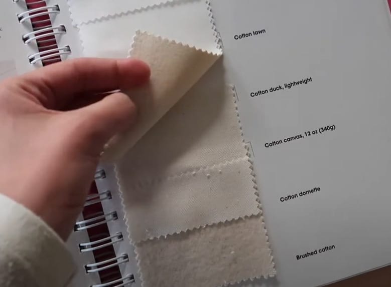 A person holding a fabric swatch in a notebook