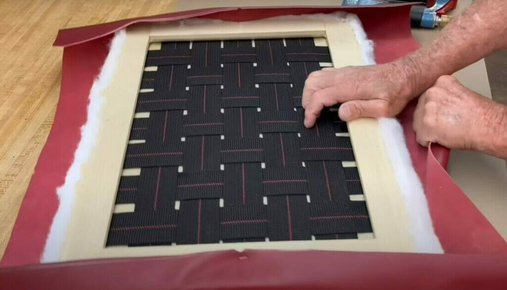 A man is demonstrating upholstery by putting a piece of fabric on a wooden frame