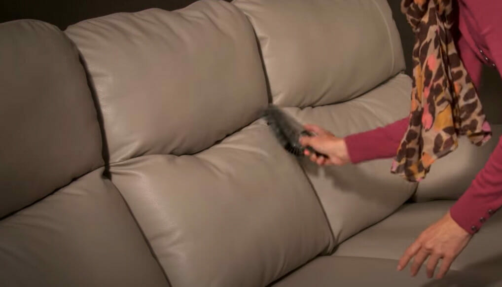 A woman cleaning leather couch with a vacuum