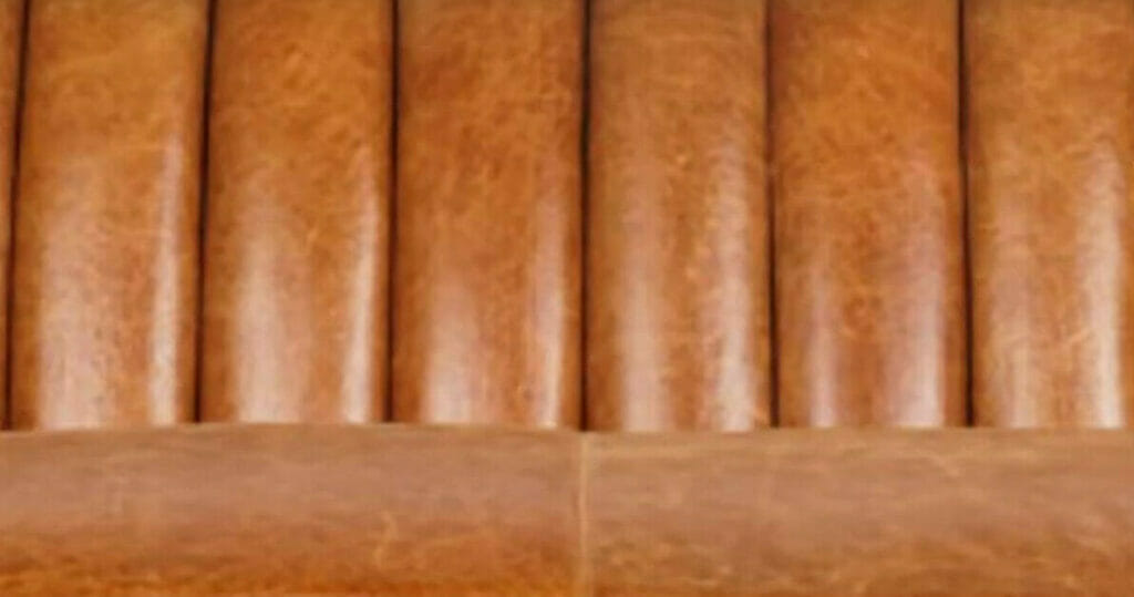 A close up of a brown leather sofa featuring channel tufting in upholstery