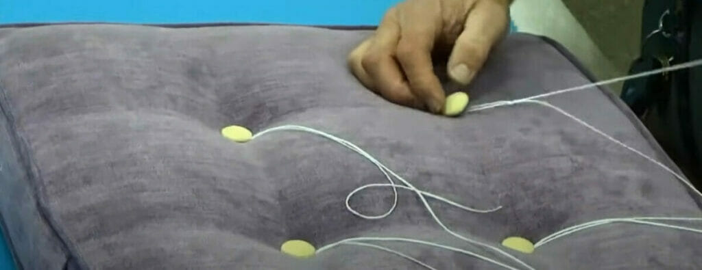 A person threading a button on the tuft cushion