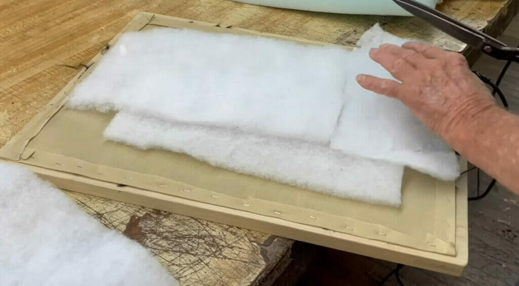 A person cutting a piece of white felt on a table for upholstery