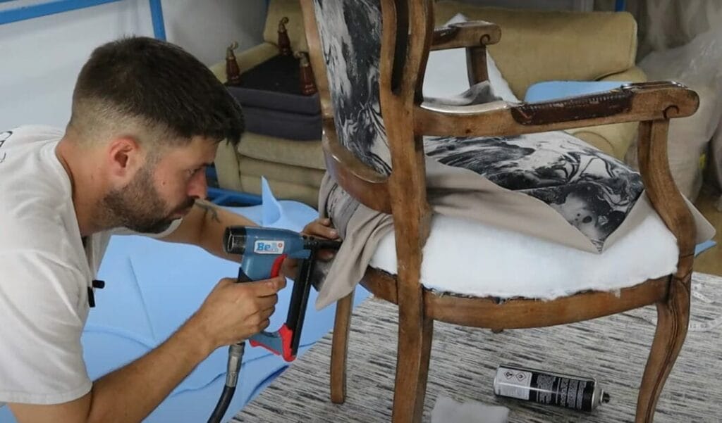 A man securing the upholstered chair using a nail gun