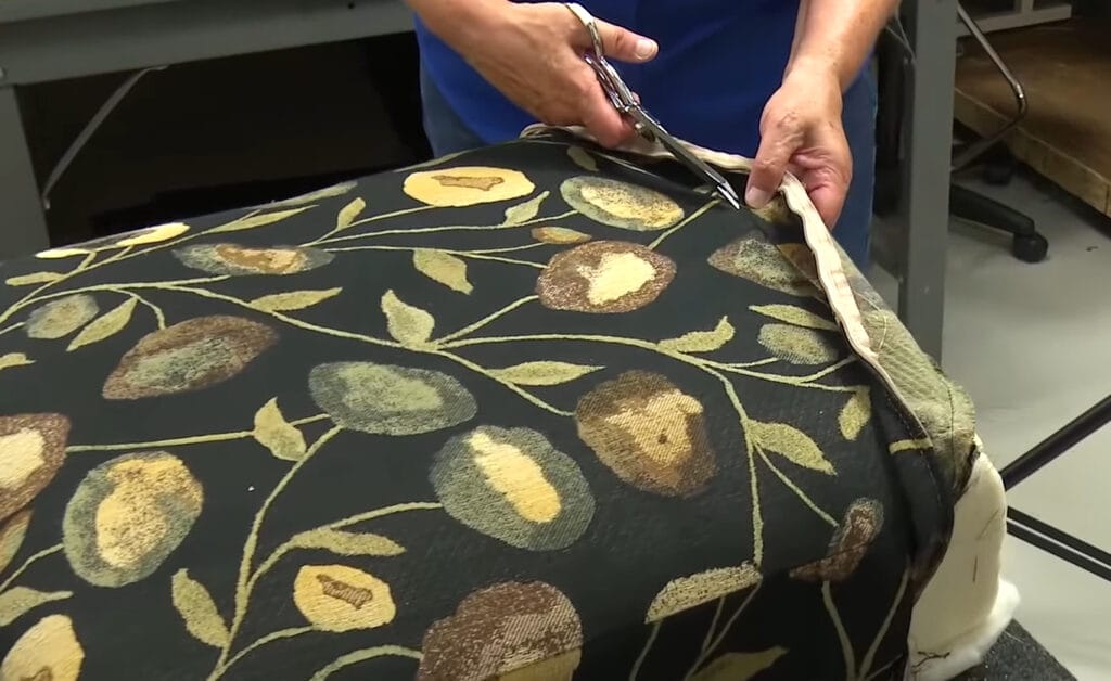 A person cutting off the old fabric on a cushion