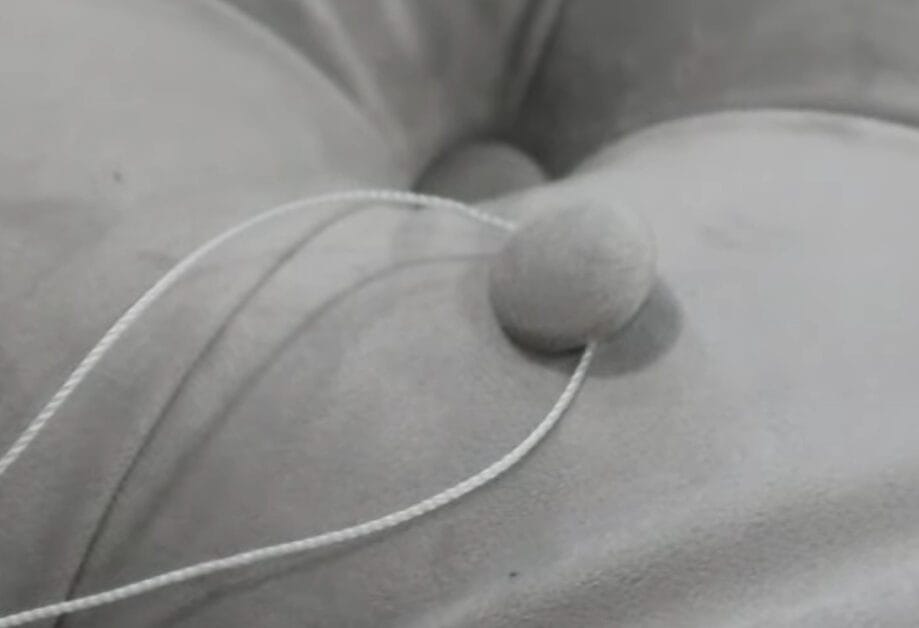A close up of a button with thread on a gray couch