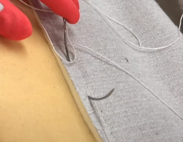 A person is using an upholstery needle and thread to stitch fabric