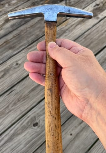 A hand holding an upholstery hammer on a wooden deck