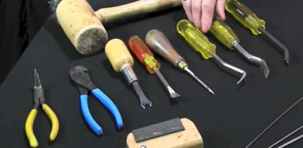 A person is showing a variety of tools for upholstery on a table