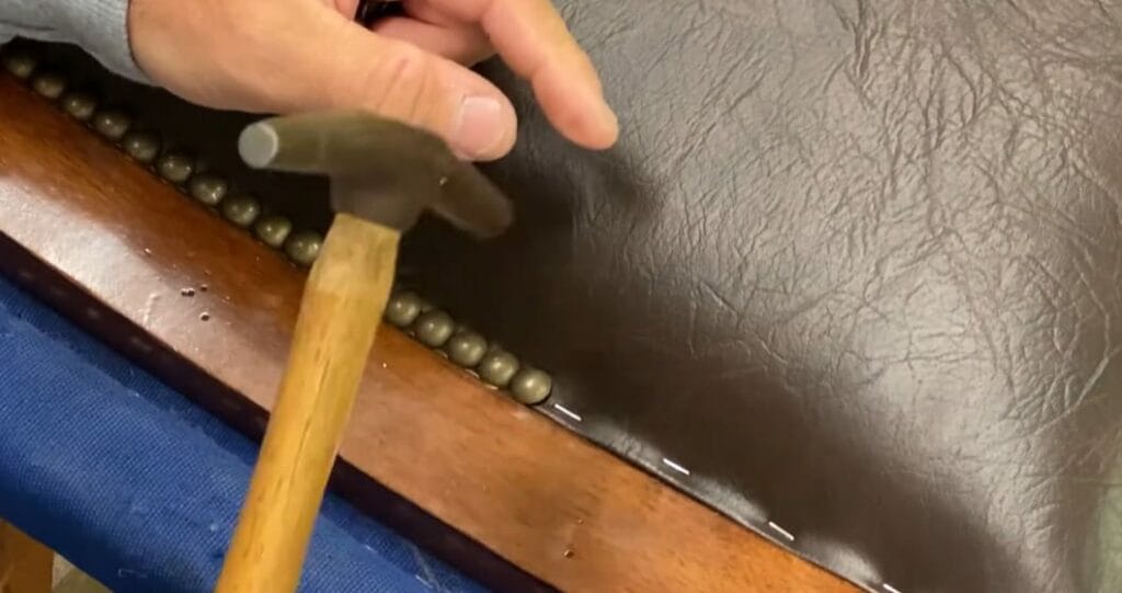 A person is using a hammer to put button nails on the edges of a leather seat