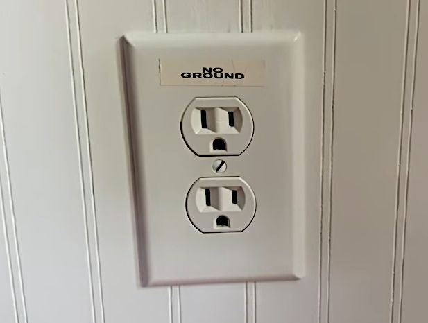 A white wall outlet with a sticker that says "NO GROUND" on it