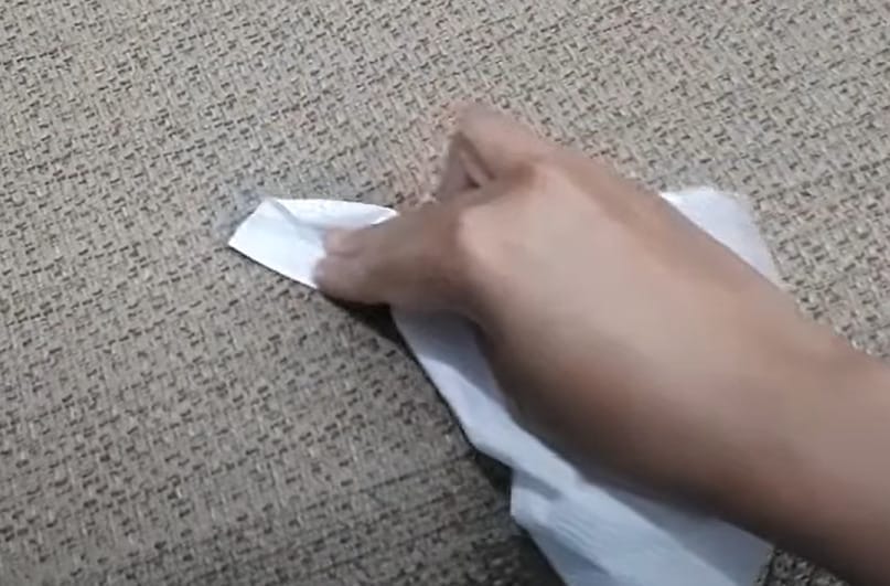 A person pressing a tissue paper into the upholstery with spilled liquid