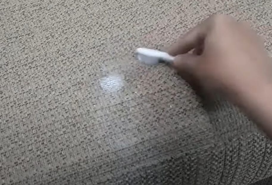 A person brushing the upholstery with a detergent-based cleaning powder