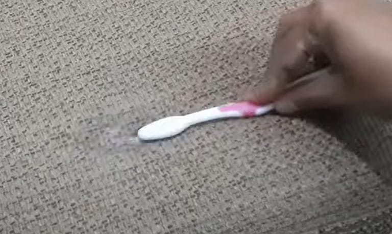 A person putting a baking soda on the upholstery with stain and brushing it