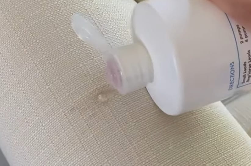 A person is using a bottle of liquid to clean a couch