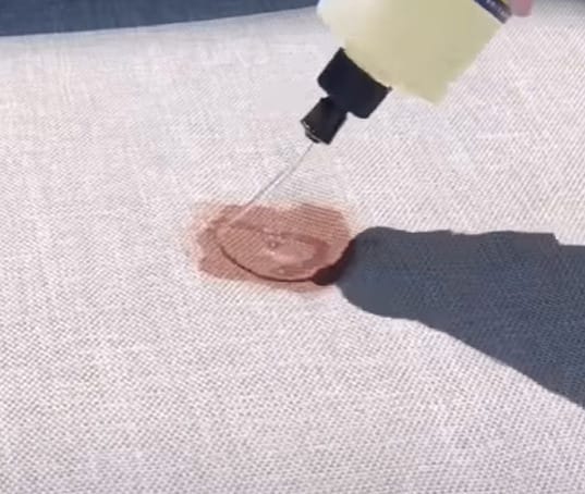 A person effectively sprays a liquid onto a piece of fabric with stain