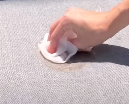 A person cleaning the stained couch with a piece of tissue with liquid solution
