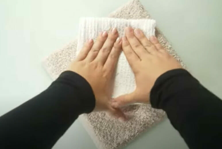 A person's hands on top of a towel demonstrating effective strategies for handling stains and spills on upholstered furniture