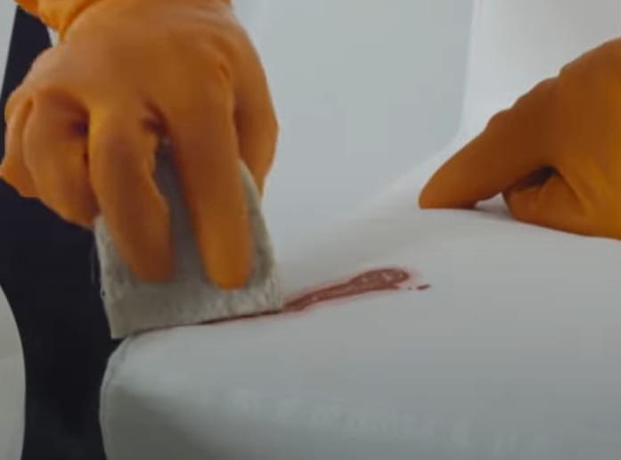 A person in orange gloves is effectively cleaning a couch with a cloth