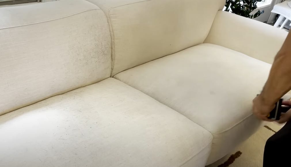 A person effectively cleaning a white couch with a vacuum.