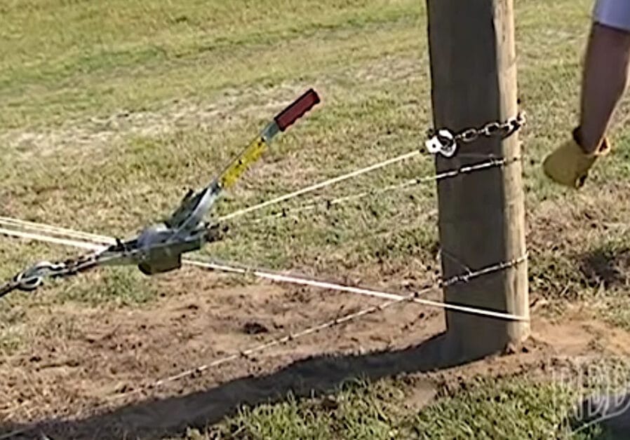 A man is installing a barbed wire fence using a tool
