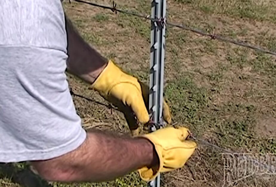 A man in yellow gloves attach the barbed wire to the intermediate posts